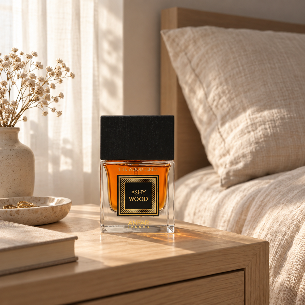 Anfar London Ashy Wood perfume bottle on a pale wooden bedside table beside linen bedding in morning light