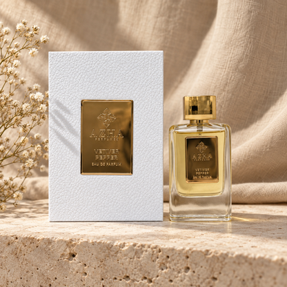 Azha Vetiver Pepper Eau de Parfum 100 ml clear glass bottle and white pebbled-leather box with gold plaque on a travertine ledge with linen backdrop